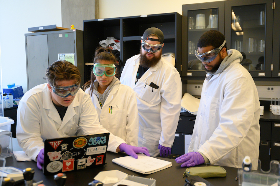 Students huddle around a lab experiment. 