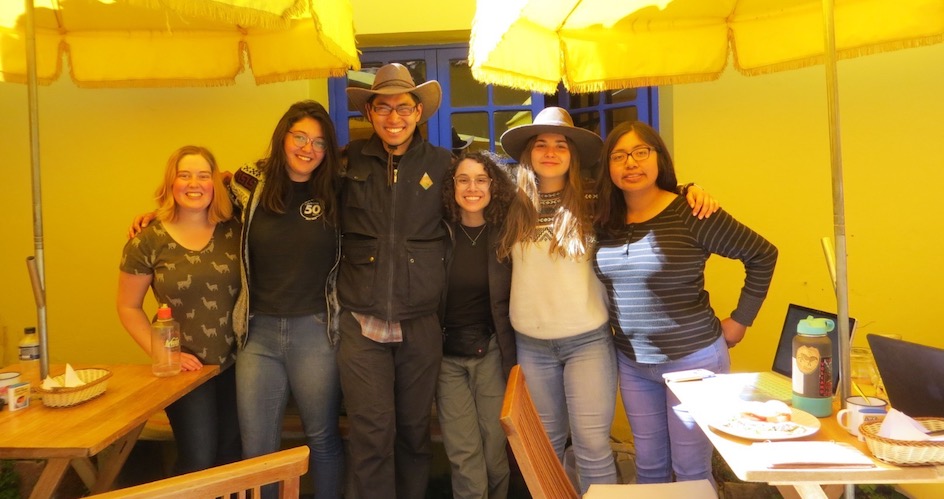 A group of students join arms inside a restaurant, alongside open laptops. 