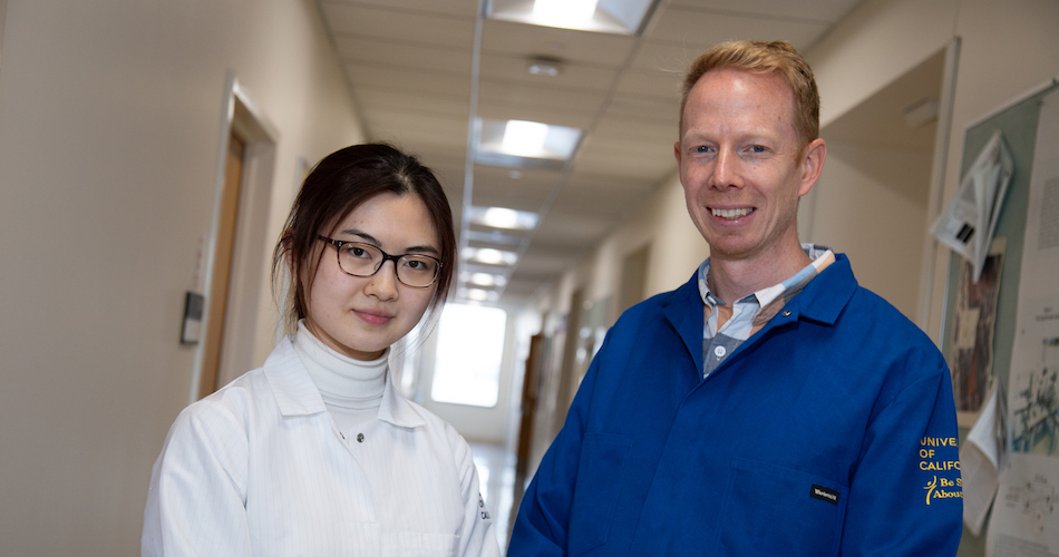 Li stands in a hallway wearing a lab coat next to her advisor. 