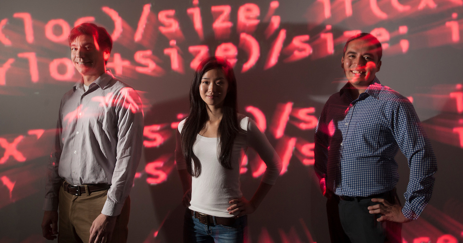 Ashley Han, a science and technology major, stands with professors Colin Milburn (left), incoming chair of the Science and Technology Department, and Gerardo Con Diaz of the Science and Technology Department. They stand in red computer code because the work that Han and Diaz have been doing is on computer programs.