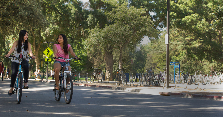 3. Managerial Economics majors Kristi Juwono (floral shirt) and Anshita Jain (pink shirt) are photographed with their bikes near the Social Sciences building on July 1, 2016. ALthough both women are from Jakarta, Indonesia, they didn't become friends until meeting at UC Davis. They are both peer advisors. Karin Higgins/UC Davis