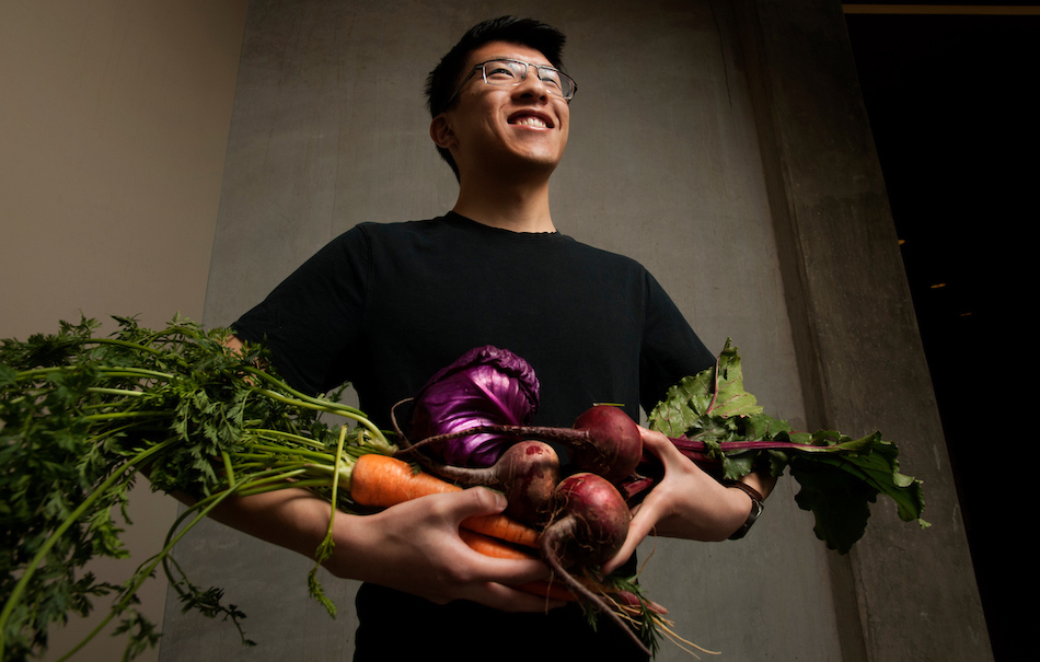 Student smiles while holding a bundle of bright vegetables.