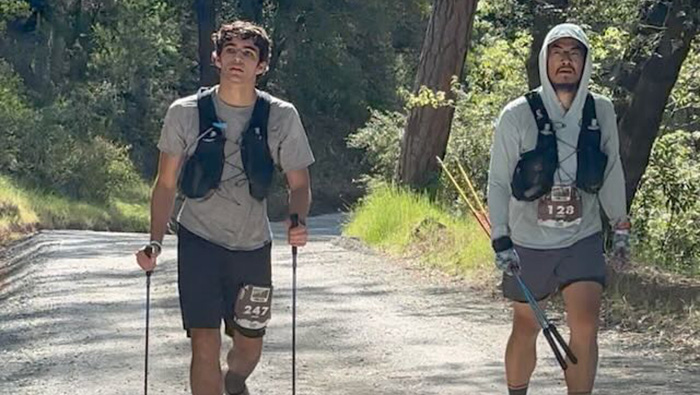 Endurance-race Ultramarathoners walk with poles in wooded area