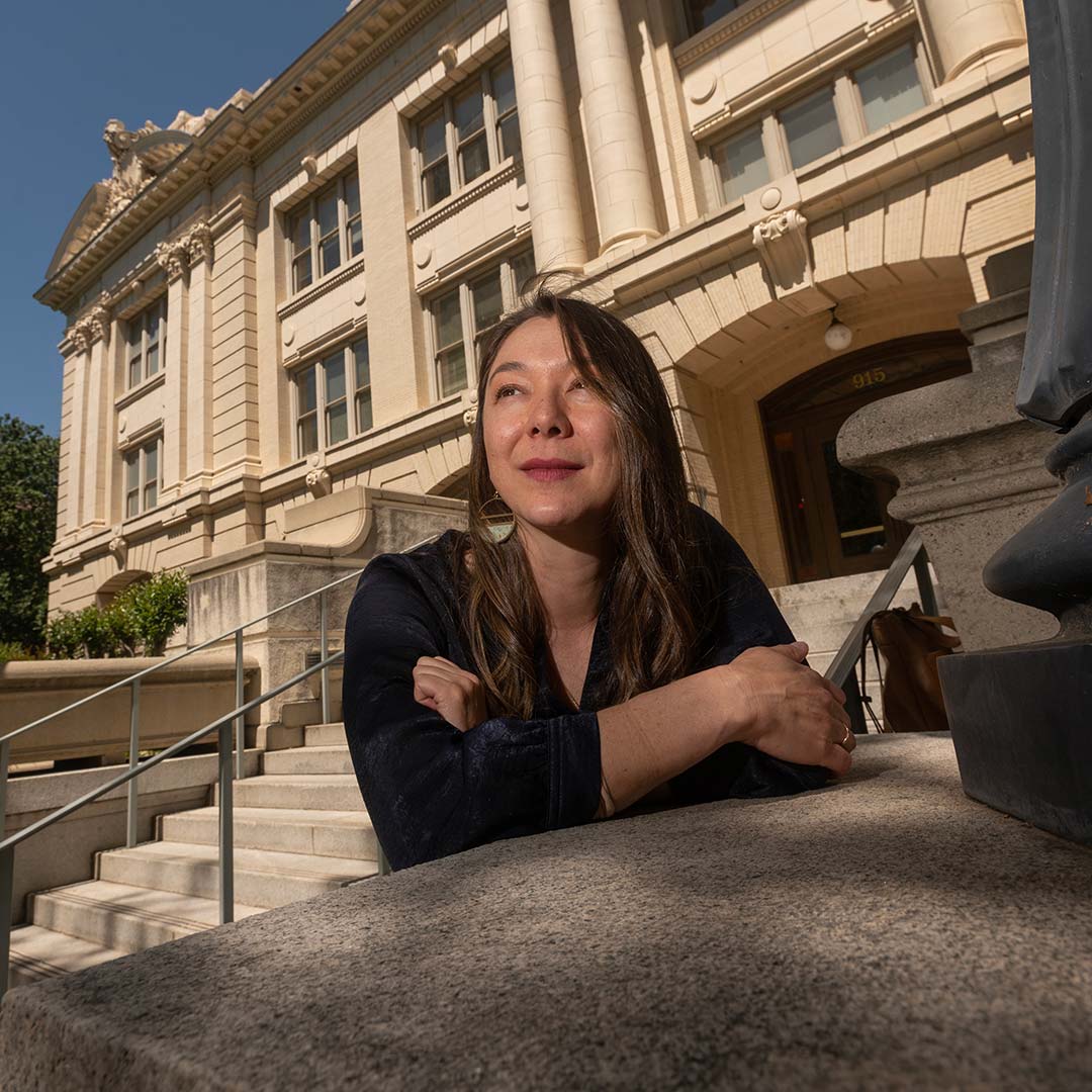 kelly-fong-rivas A woman stands on the steps outside the front of Sacramento City Hall and looks off camera. She is wearing a black blazer.