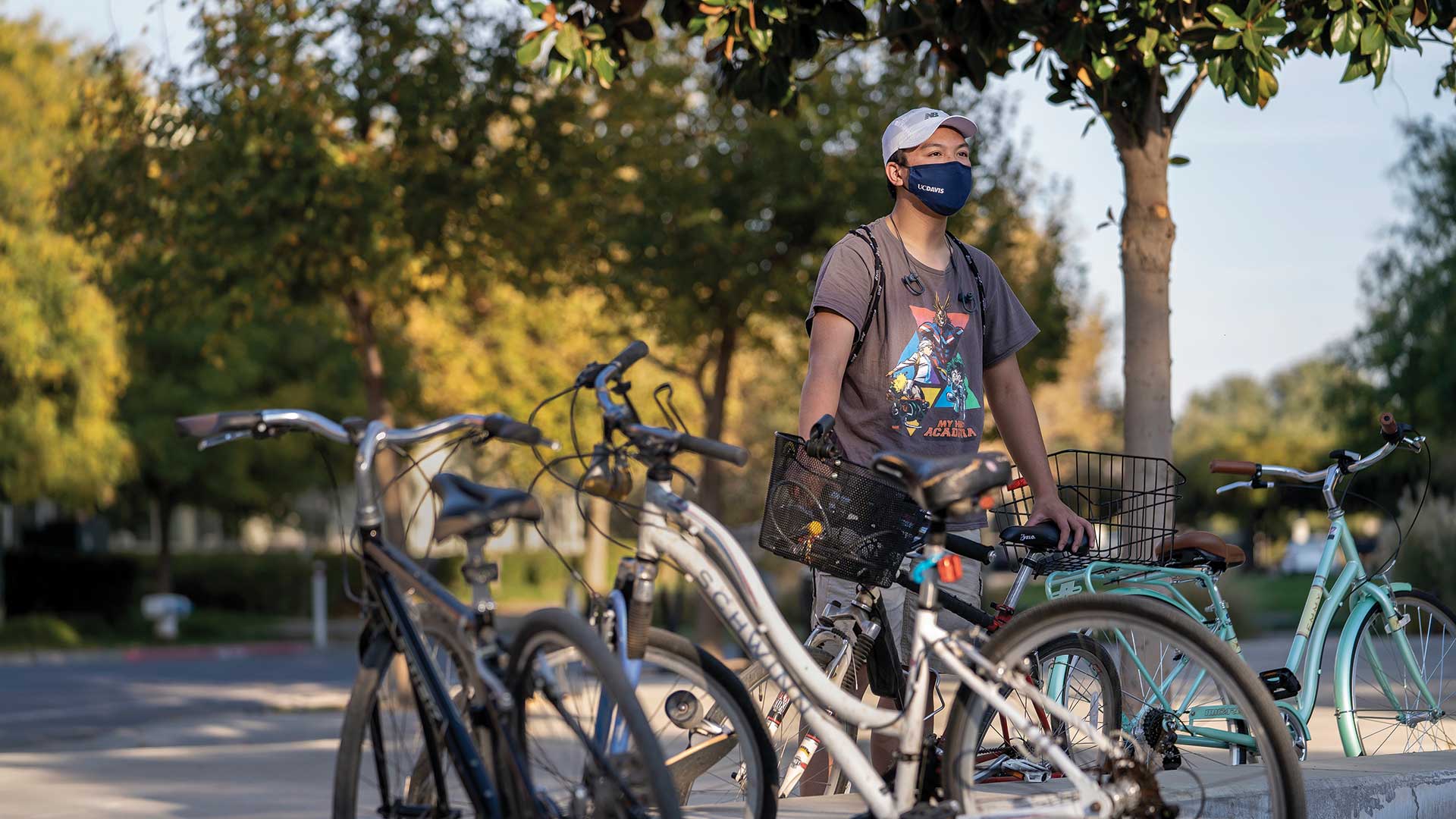 portraits-wong A student stands with bikes on campus and wearing a face mask