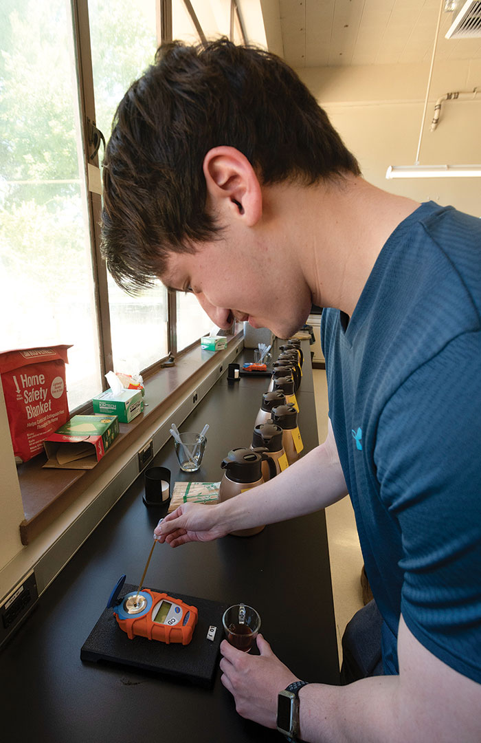 A student watches as they pipette drops of coffee on to an electronic lab instrument's sensor.