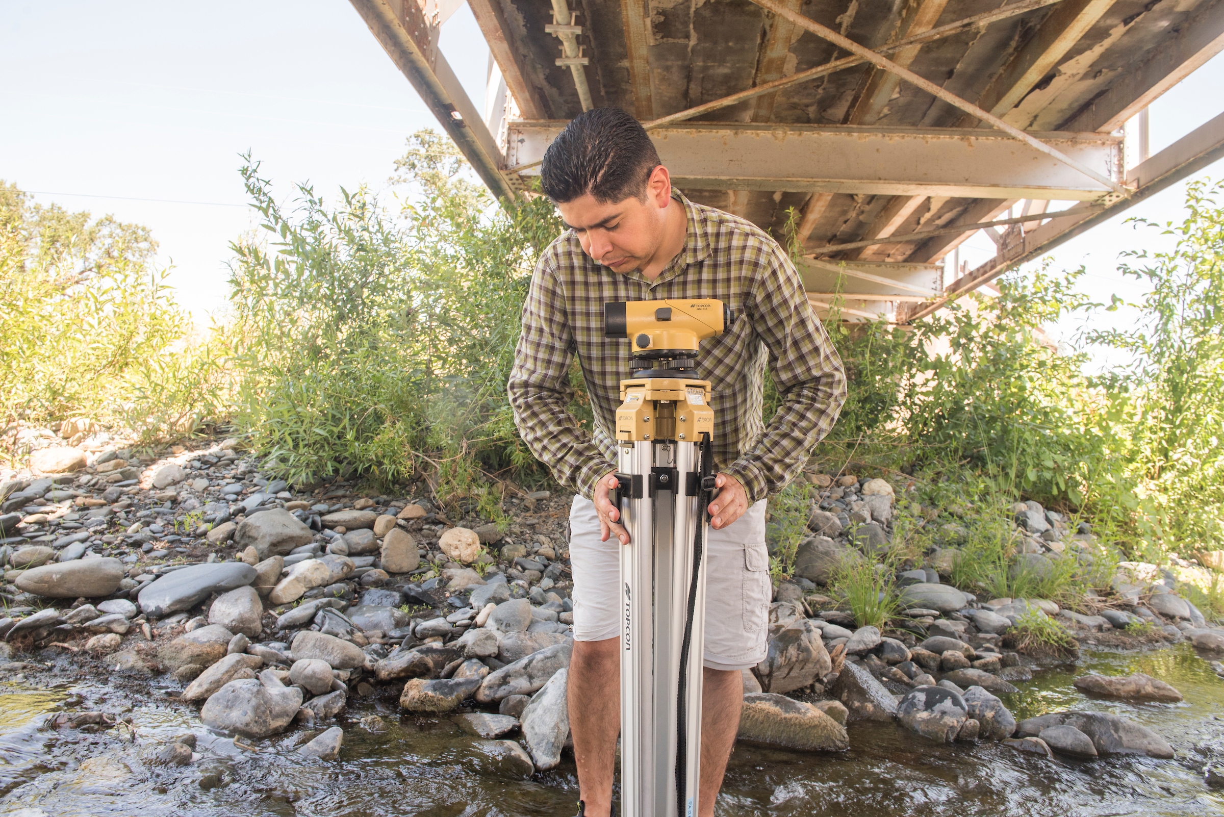 Man beneath bridge by a stream folds water-collection gear. 