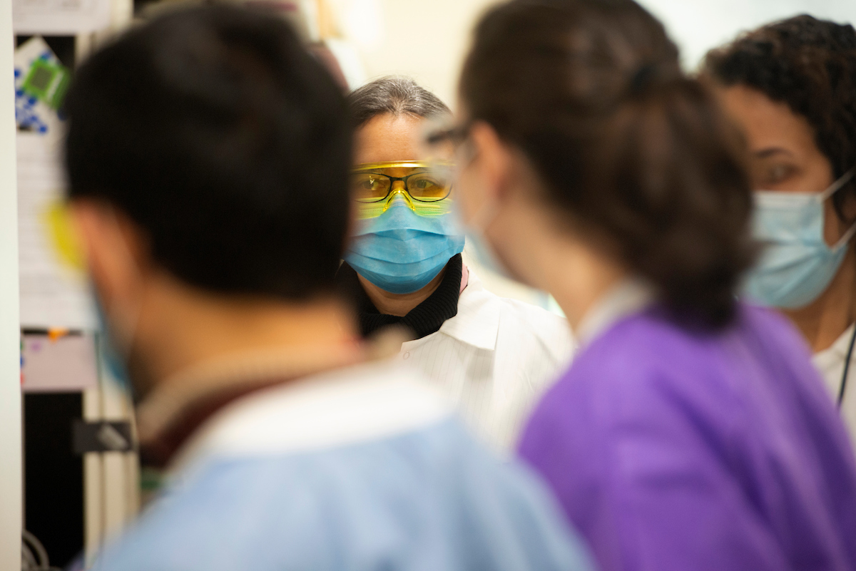 Woman scientist with mask surrounded by blurry images of other masked scientists