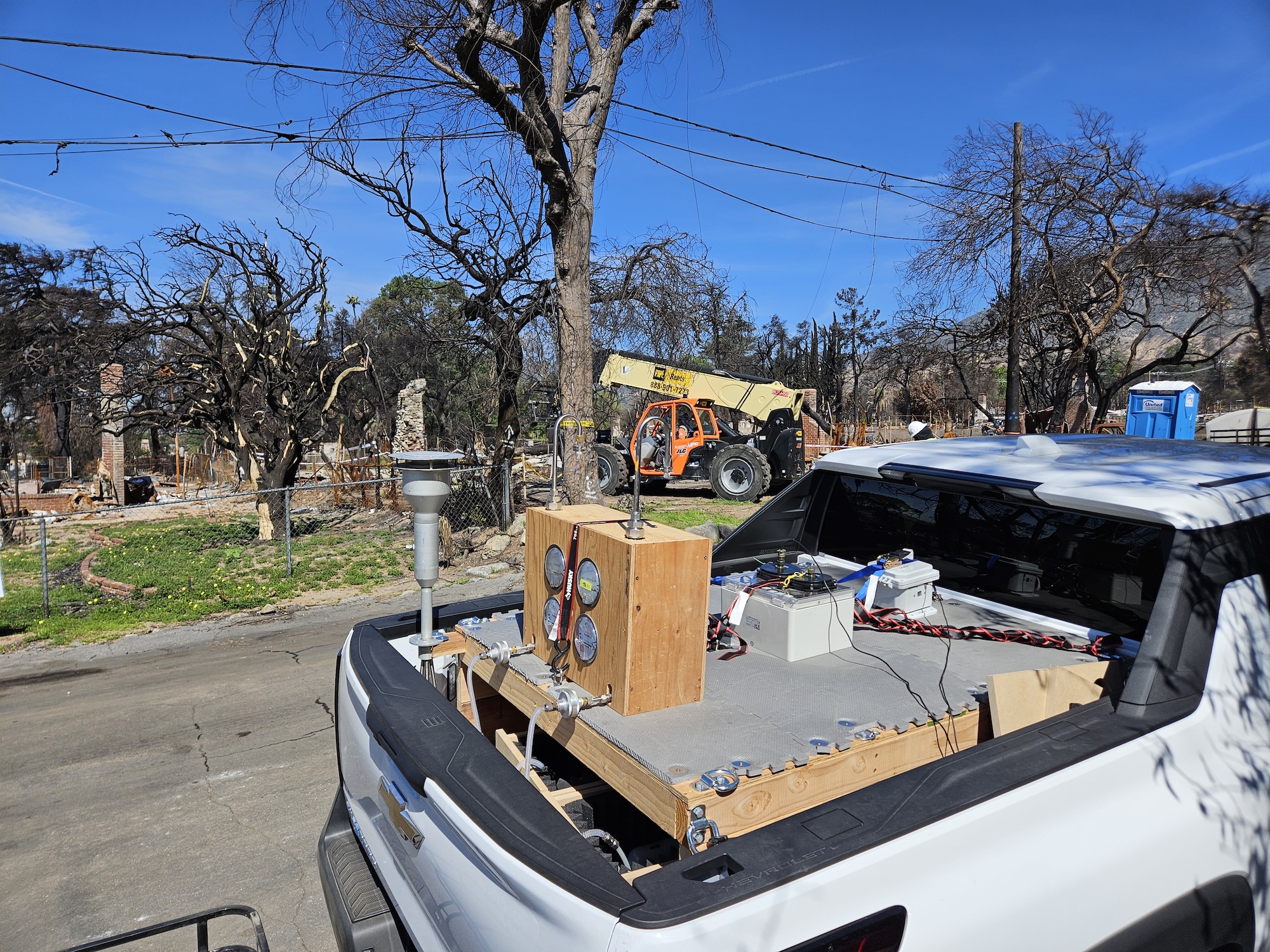 white truck full of air sampling equipment drives along burned trees on a site affected by 2025 Los Angeles fires