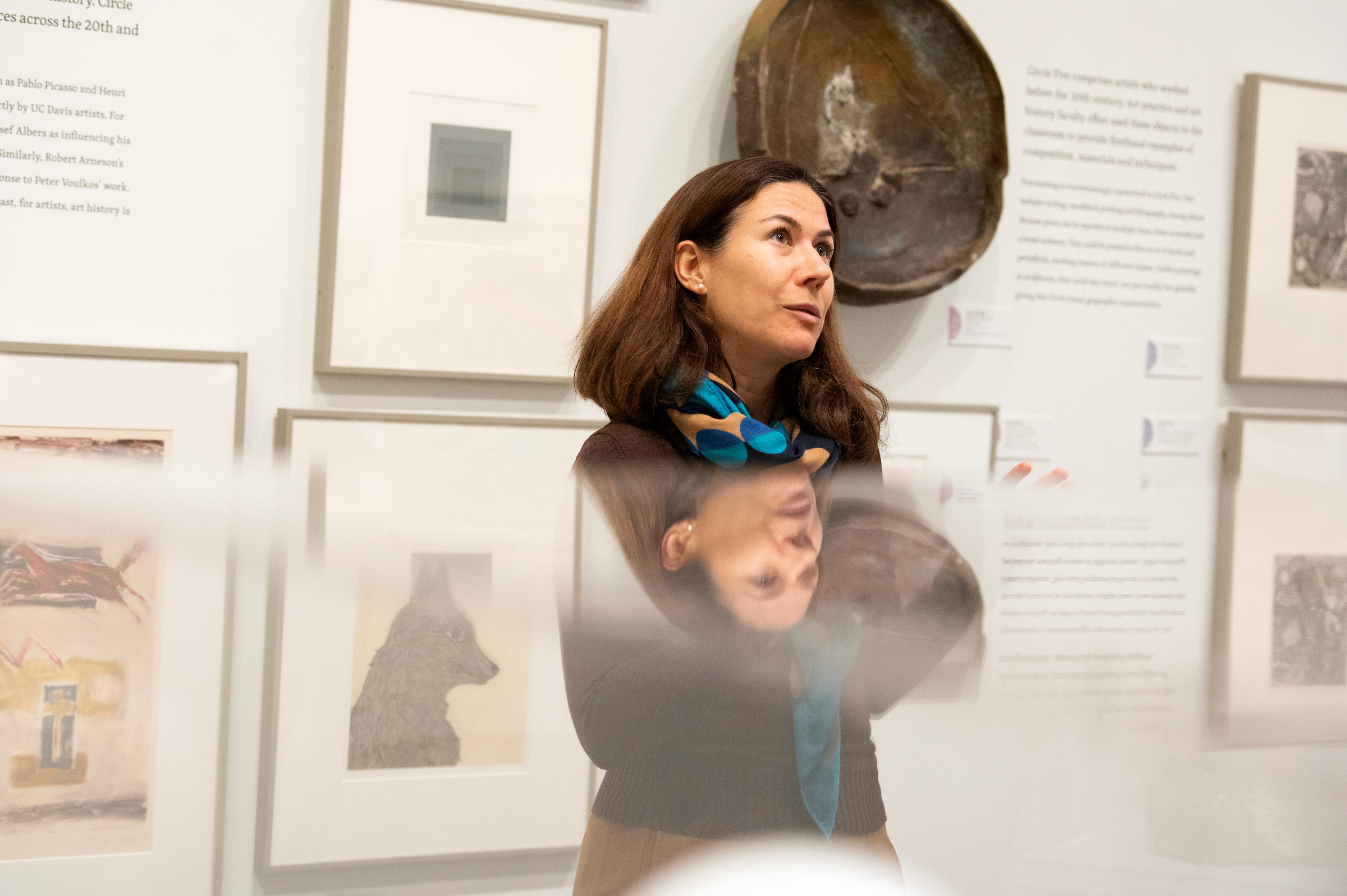 A woman with long dark hair stands in an art gallery, surrounded by framed artworks.