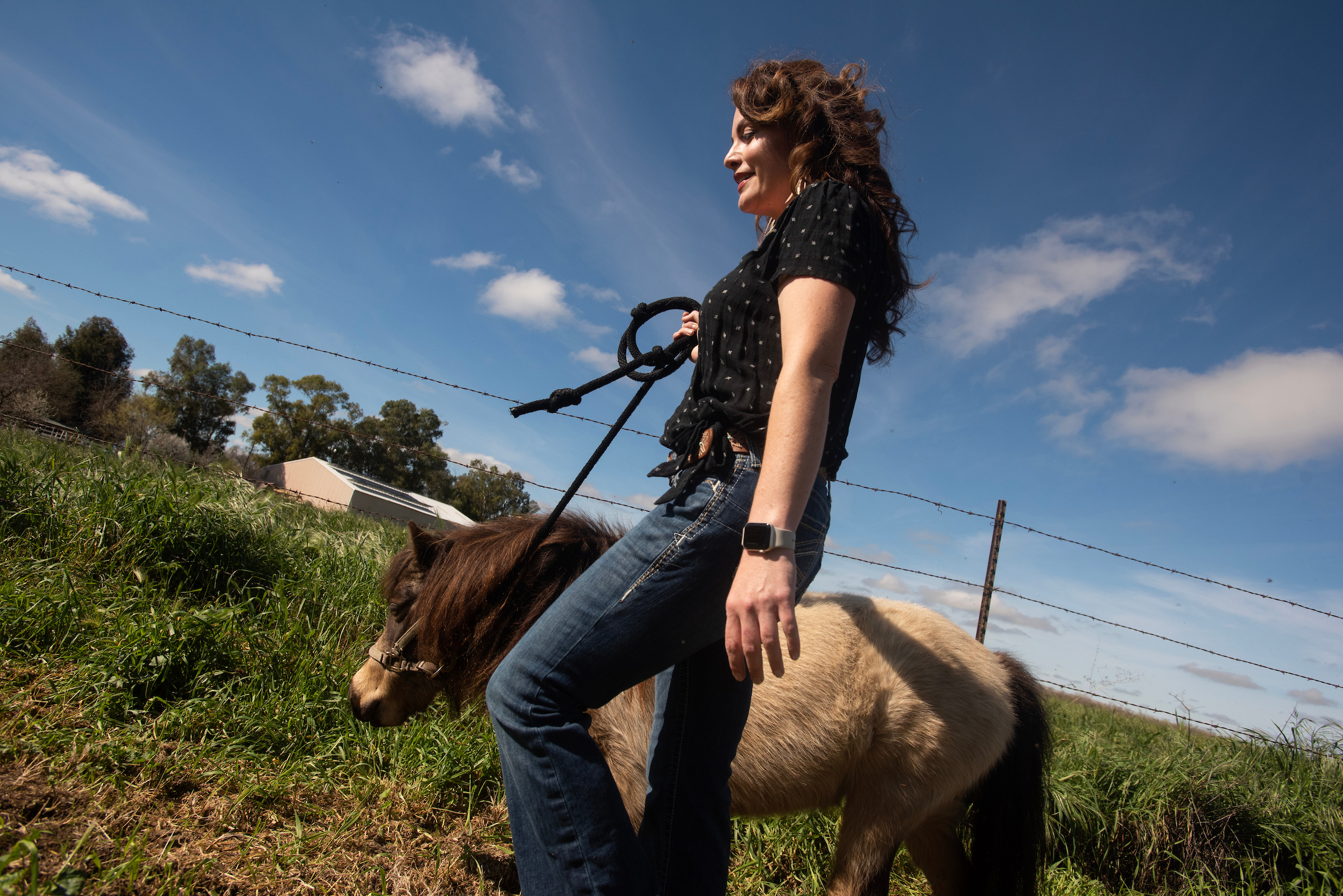 Rebecca Calisi Rodríguez in black shirt holding reins of small brown-and-white horse in grassy field