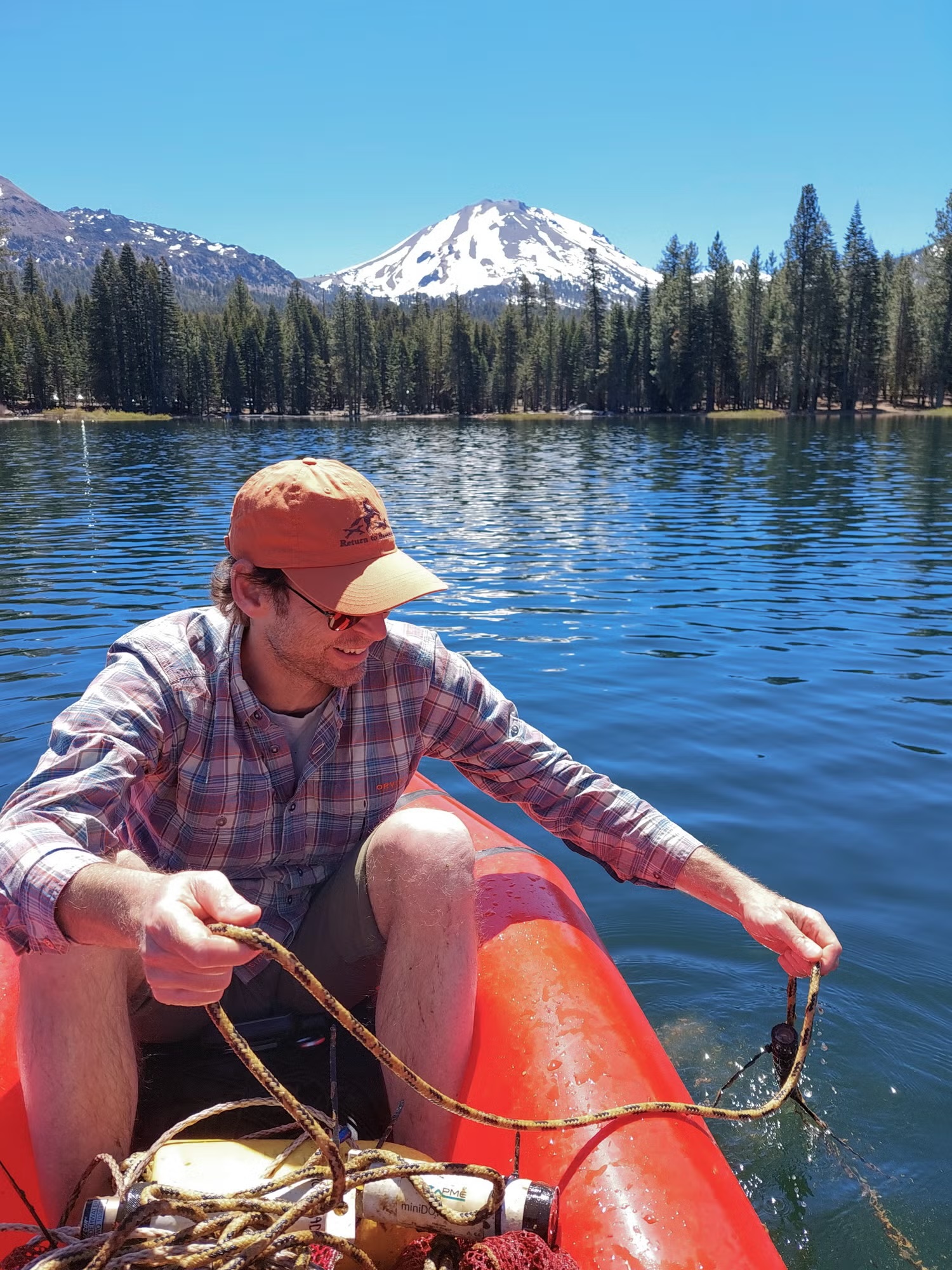 Man in orange cap in red canoe on clear alpine lake with snow-capped peak
