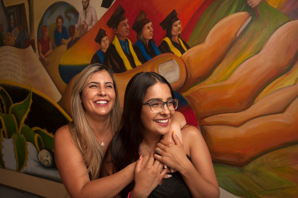A mother and daughter smile in front of a mural.