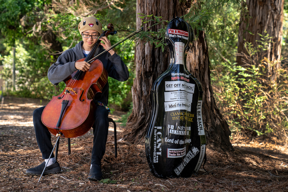 A student plays cello in the woods at UC Davis.