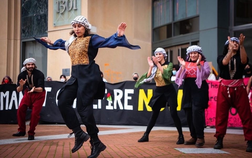 Masked dancers performing outdoors; central dancer jumps with arms raised