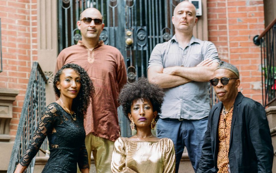 A diverse group of five people poses on steps in front of a brick building.