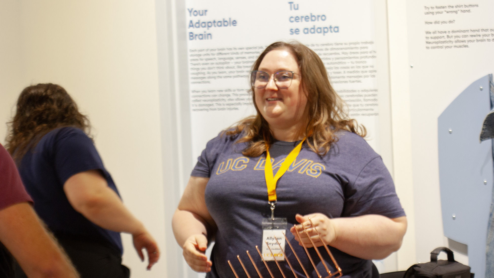 Smiling woman with glasses and yellow lanyard in an exhibition space