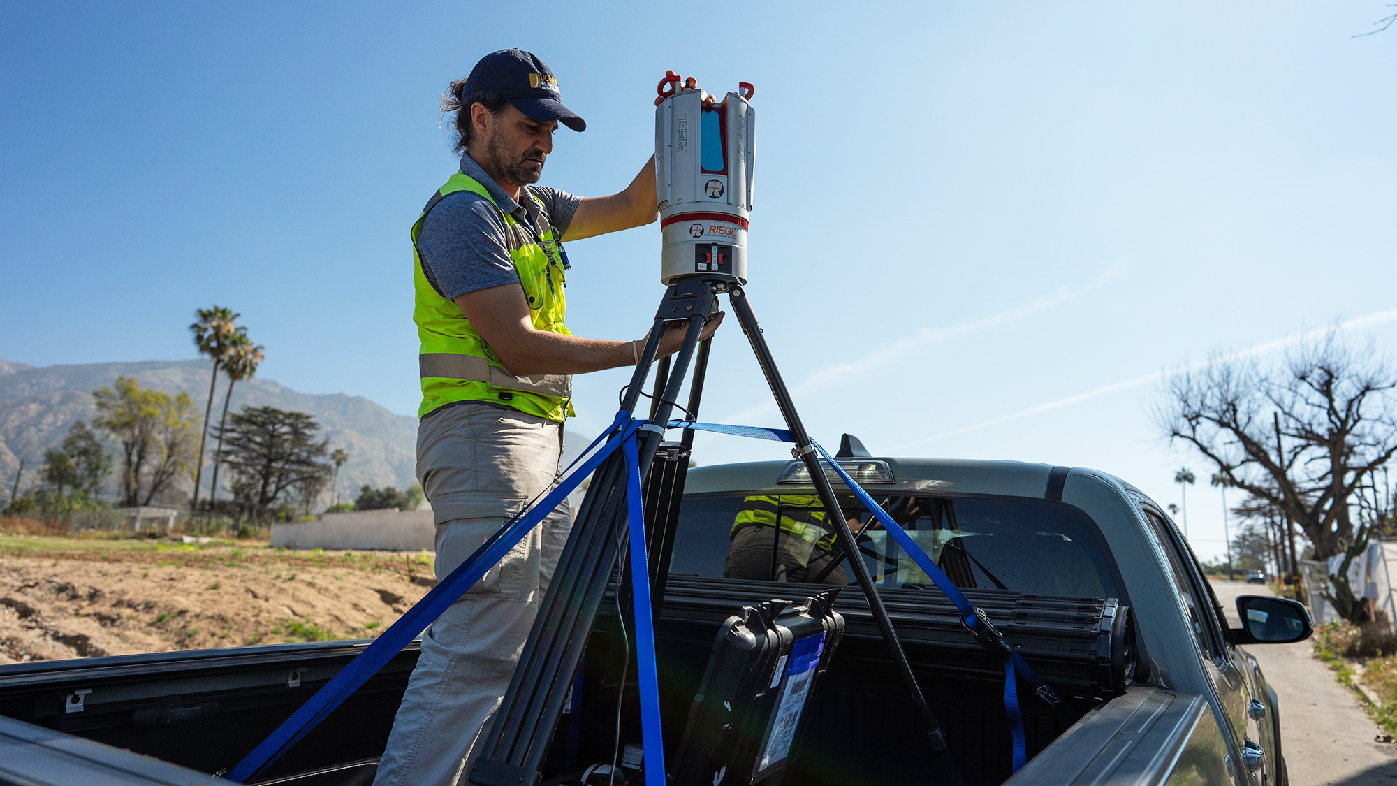 Researcher in a yellow vest operating tripod-mounted lidar scanner in pickup truck bed