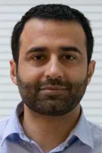 Male headshot, short dark hair and beard, light blue shirt, neutral background