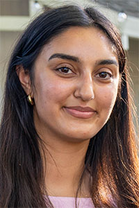 Smiling young woman with long dark hair, gold hoop earrings, soft outdoor lighting