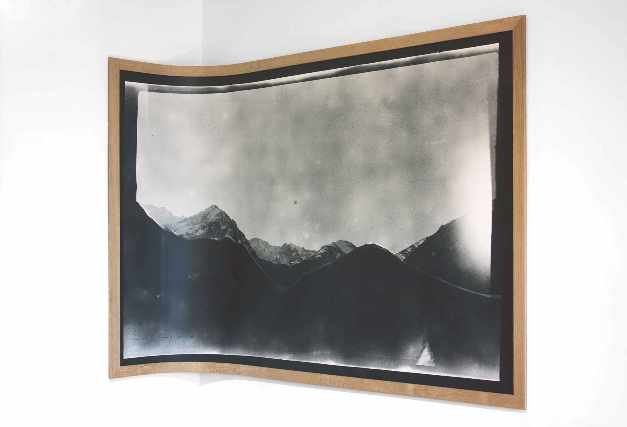 Curved monochrome photograph of mountains displayed in a wooden frame on a white wall.