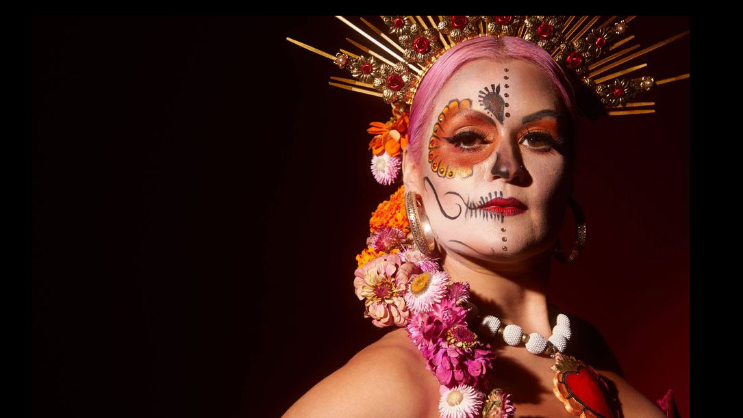 Woman in costume and mask, in oranges and red, on dark background