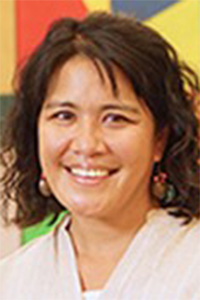 Smiling woman with curly hair, wearing earrings, against a colorful abstract background.