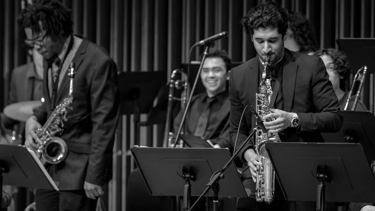 Black-and-white photograph: three jazz saxophonists in suits on stage, smiling drummer