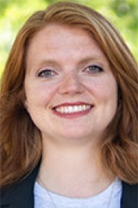 Smiling red-haired woman headshot outdoors, wearing dark blazer and white top