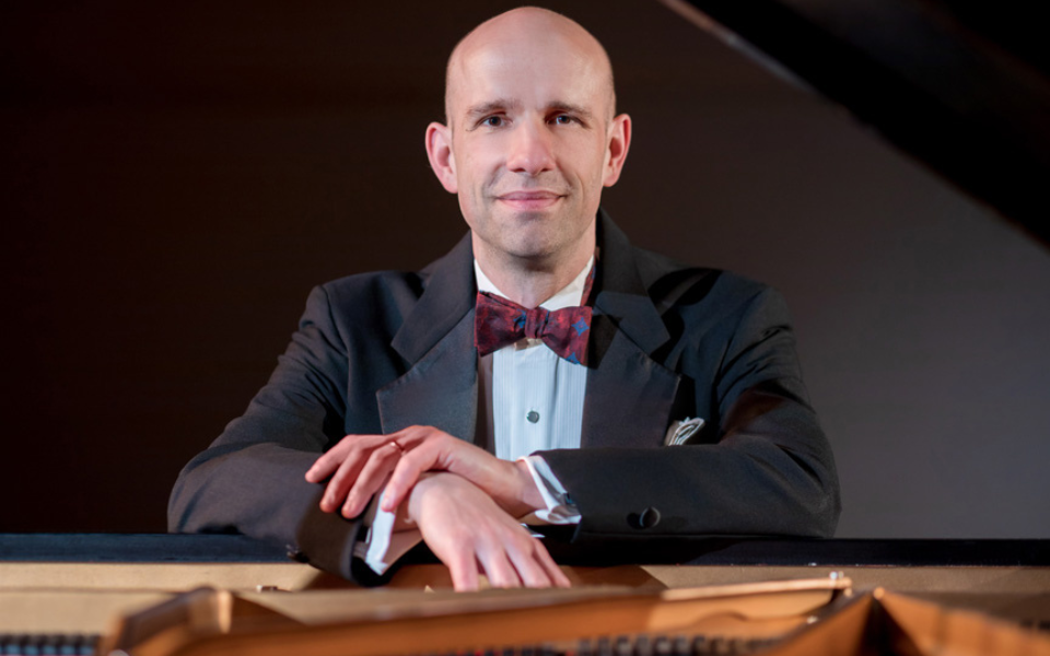 Portrait of a bald man in tuxedo with bow tie, hands on a grand piano