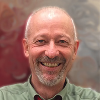 Grinning white man, balding with short grey hair and grey facial hair, wearing a green shirt. 