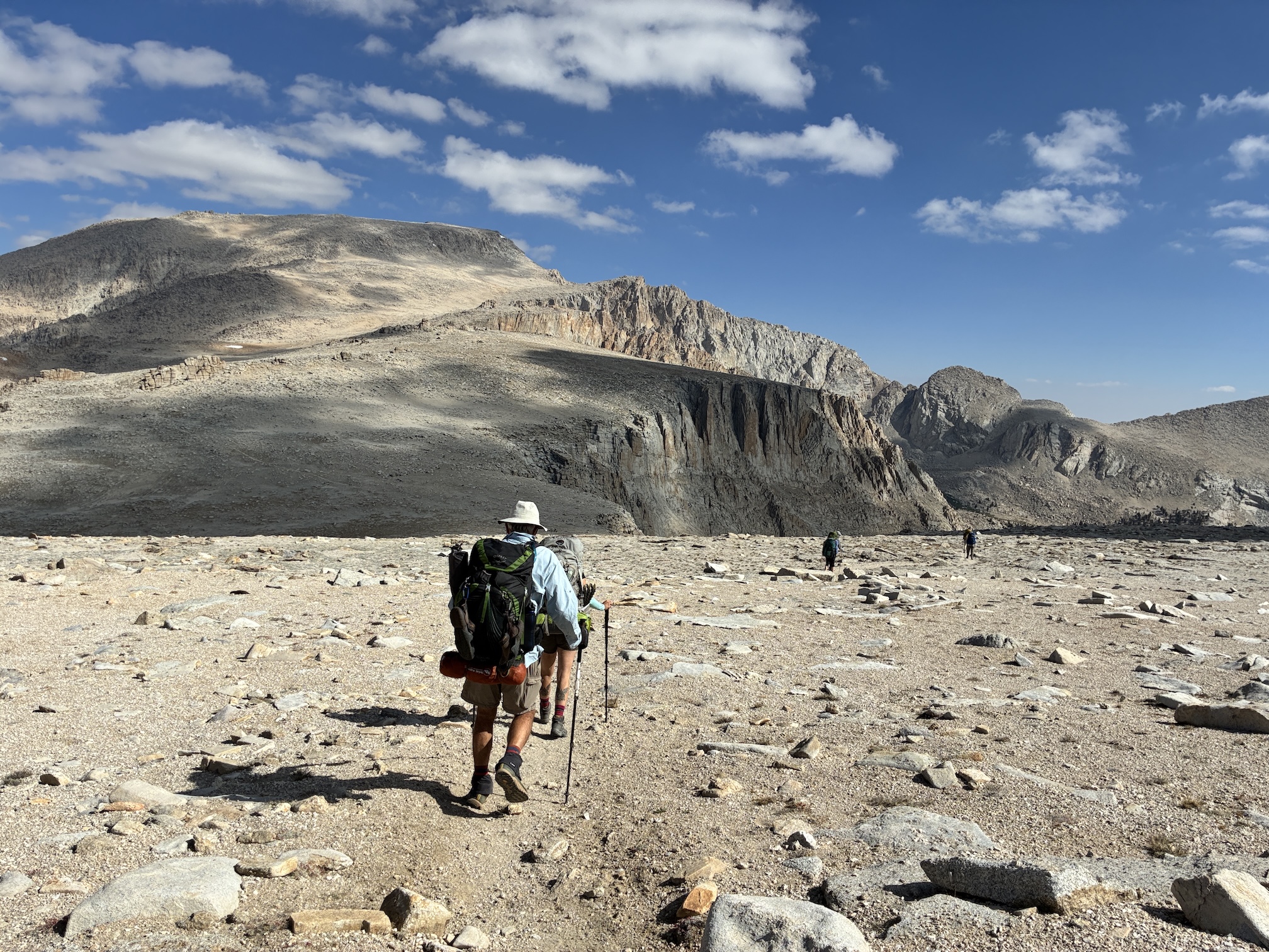 Hikers walk with pole and packs across arid rocky landscape in Sierra Nevada mountains