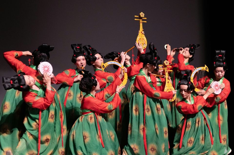 Group of traditional dancers on stage in red tops and green skirts waving fans