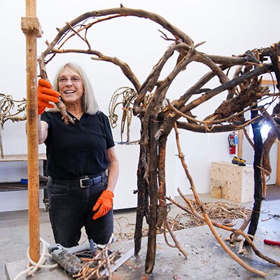 Light-complected, blond woman in black clothing stands in front of sculpture