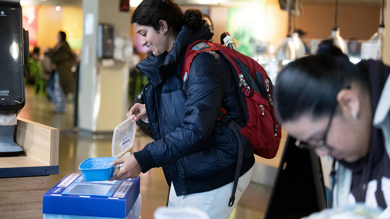 A student deposits a reusable container into a bin for pick up and washing.