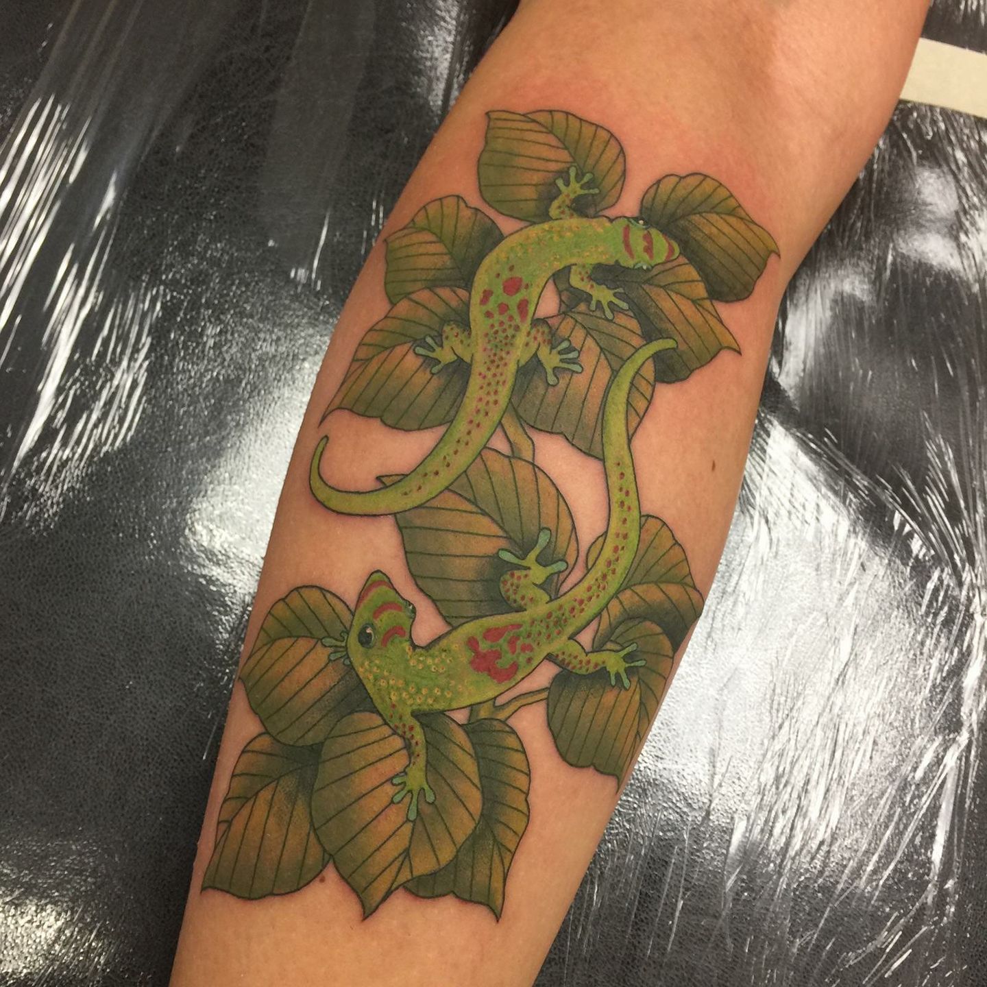 Tattoo of two green geckos with red patterns on their backs