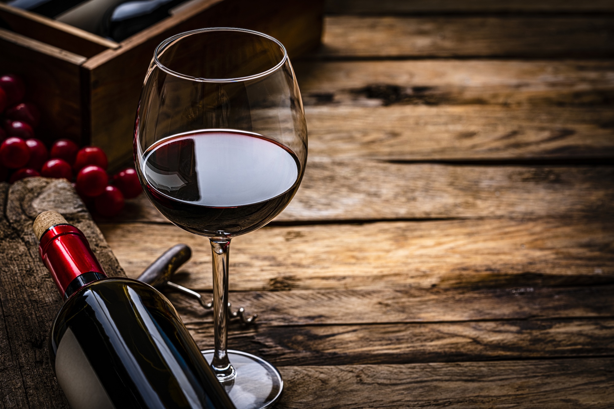 Close up view of a red wineglass shot on rustic wooden table. A wine bottle is laying beside the wineglass. Selective focus on the wineglass. A corkscrew, grapes and a wine bottle box complete the composition. (Getty)