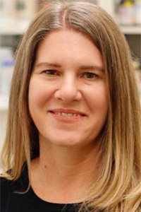 Smiling woman with long hair, wearing a black top against a blurred background.
