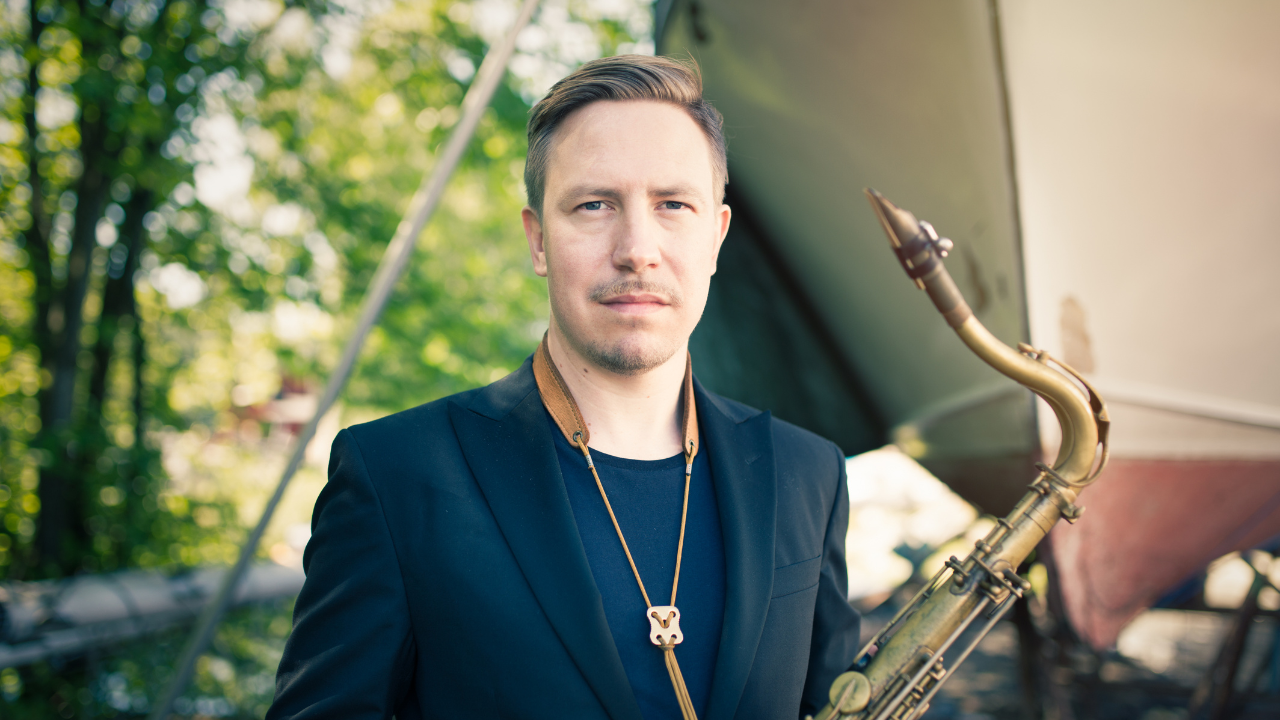 Portrait photo of a man holding a tenor saxophone outdoors, neutral expression
