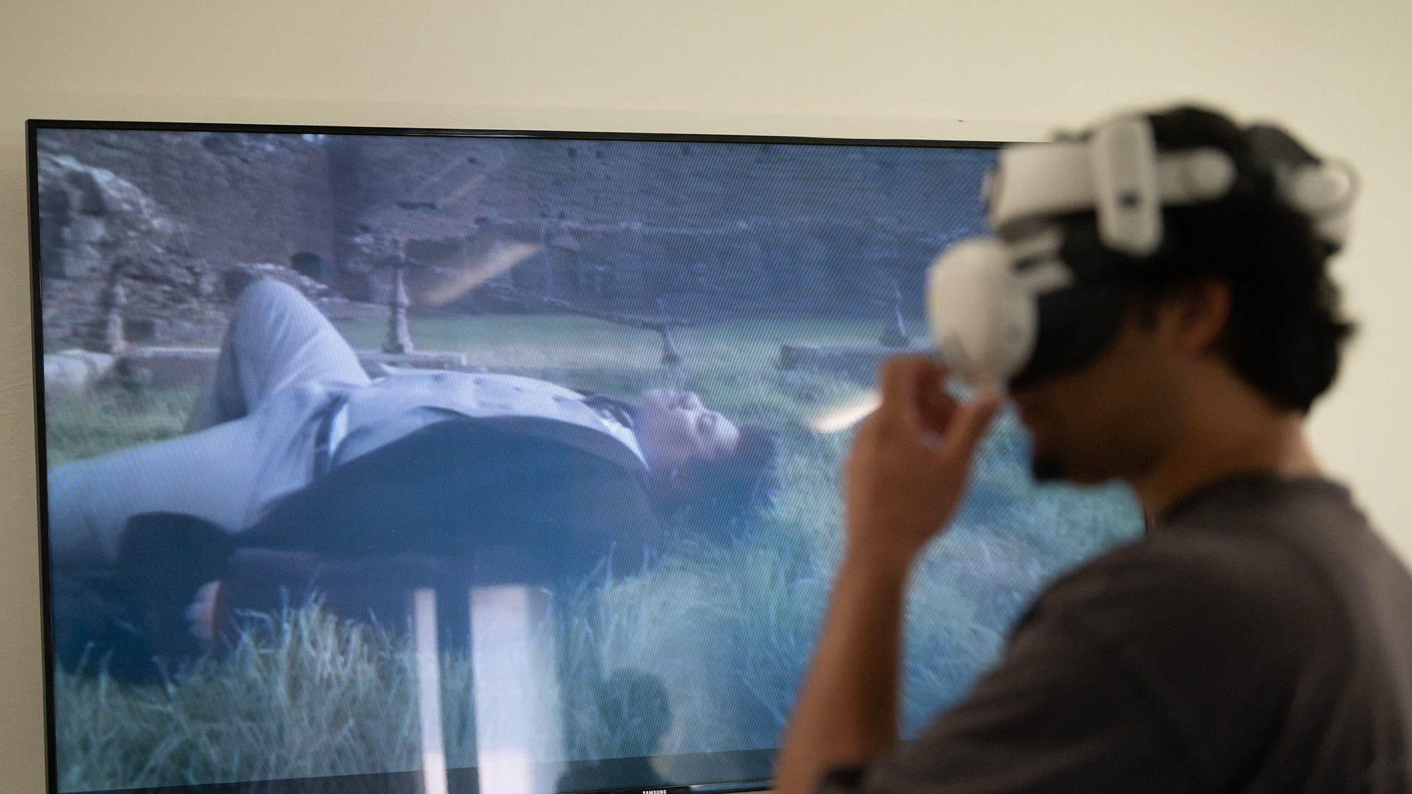 Person wearing VR headset watching a large screen showing person lying on the ground