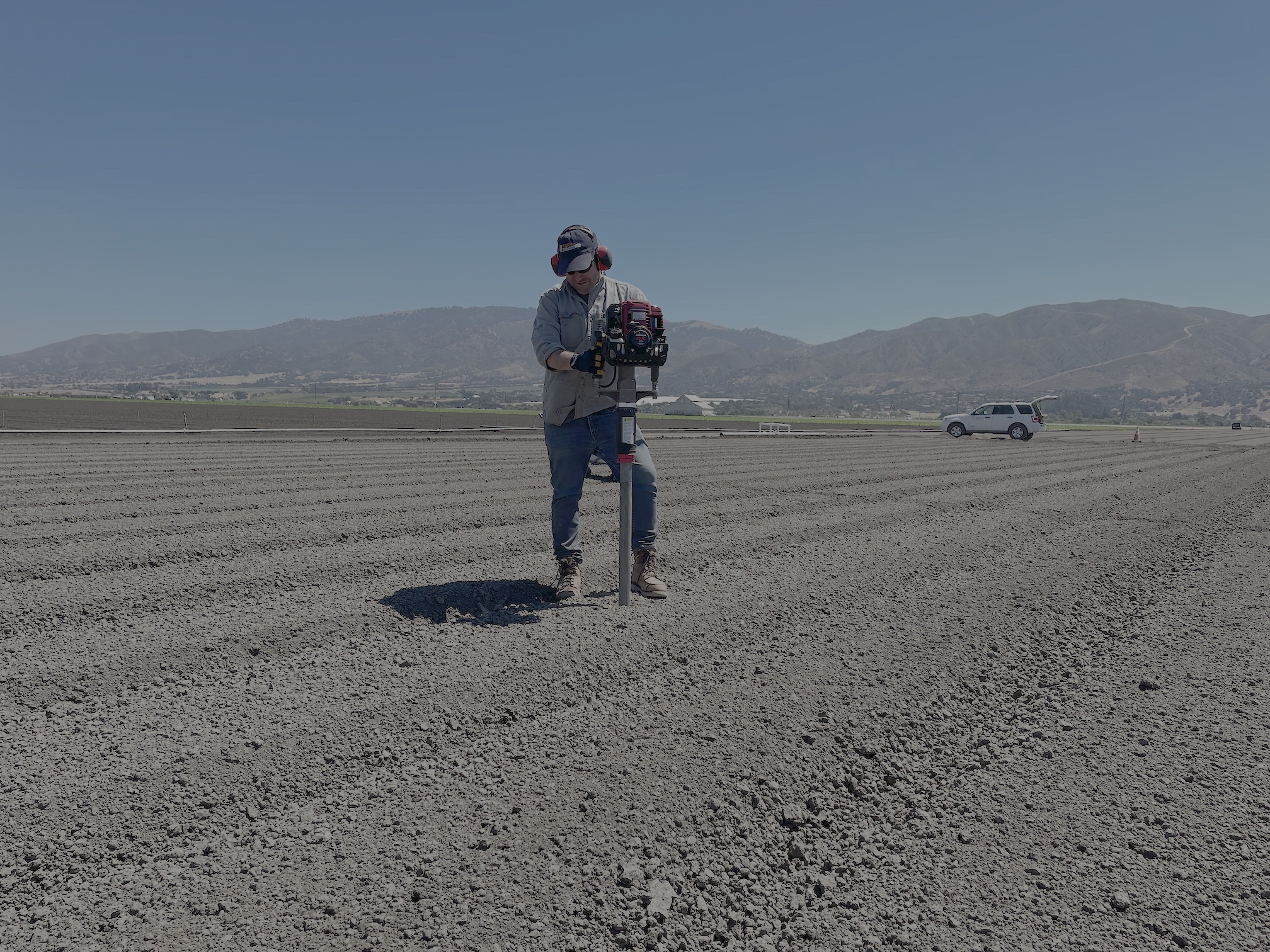 Cole Smith of UC Davis walking on plowed field carrying gear in front of mountains under a clear blue sky