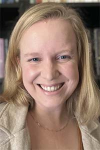 Portrait photograph of a smiling blonde woman, bookshelf background