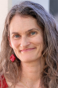 Smiling woman with long wavy gray hair and red leaf earring, headshot