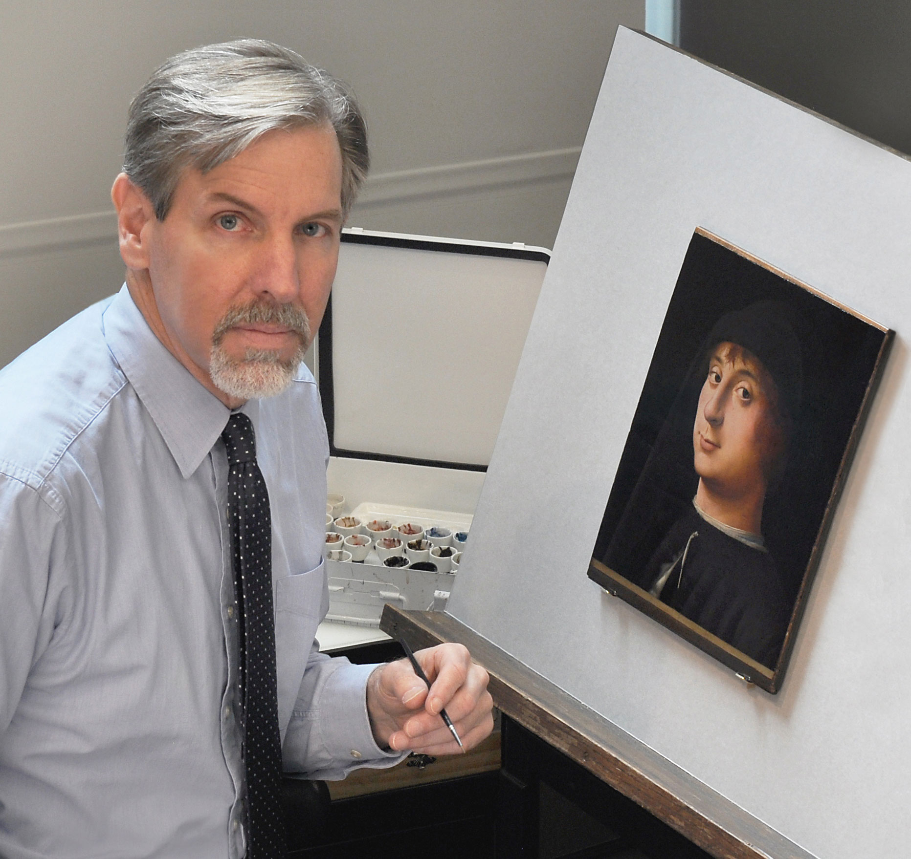 Conservator with gray hair restoring a small framed portrait on an easel