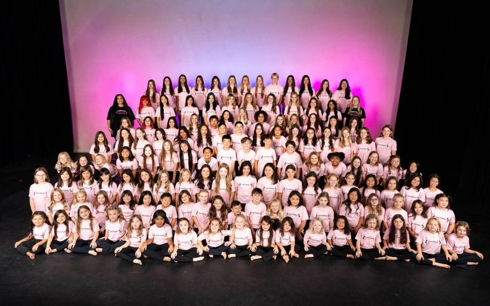 Large group of smiling students on tiered stage under pink lighting (photo)