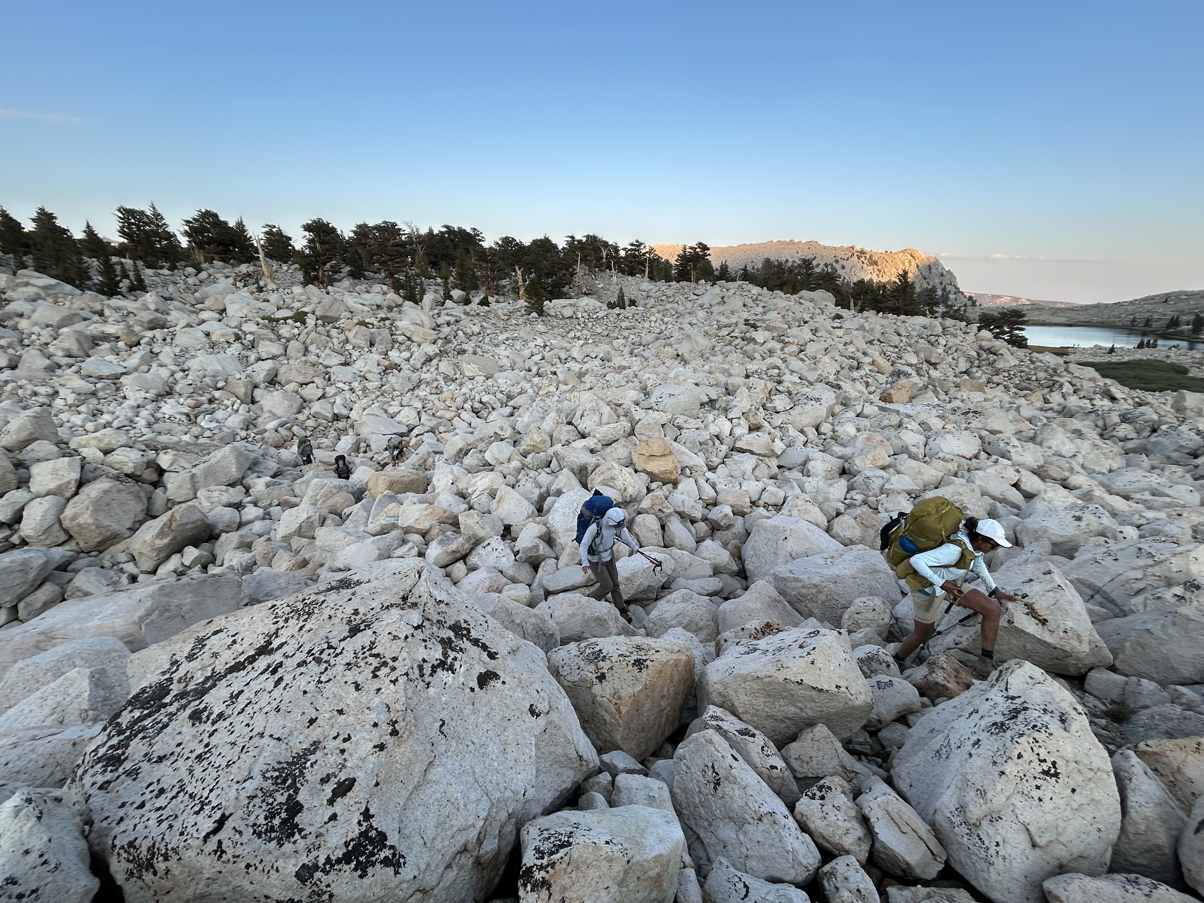 A man and woman hunch over while traversing a large boulder field in the eastern Sierra Nevada mountains 