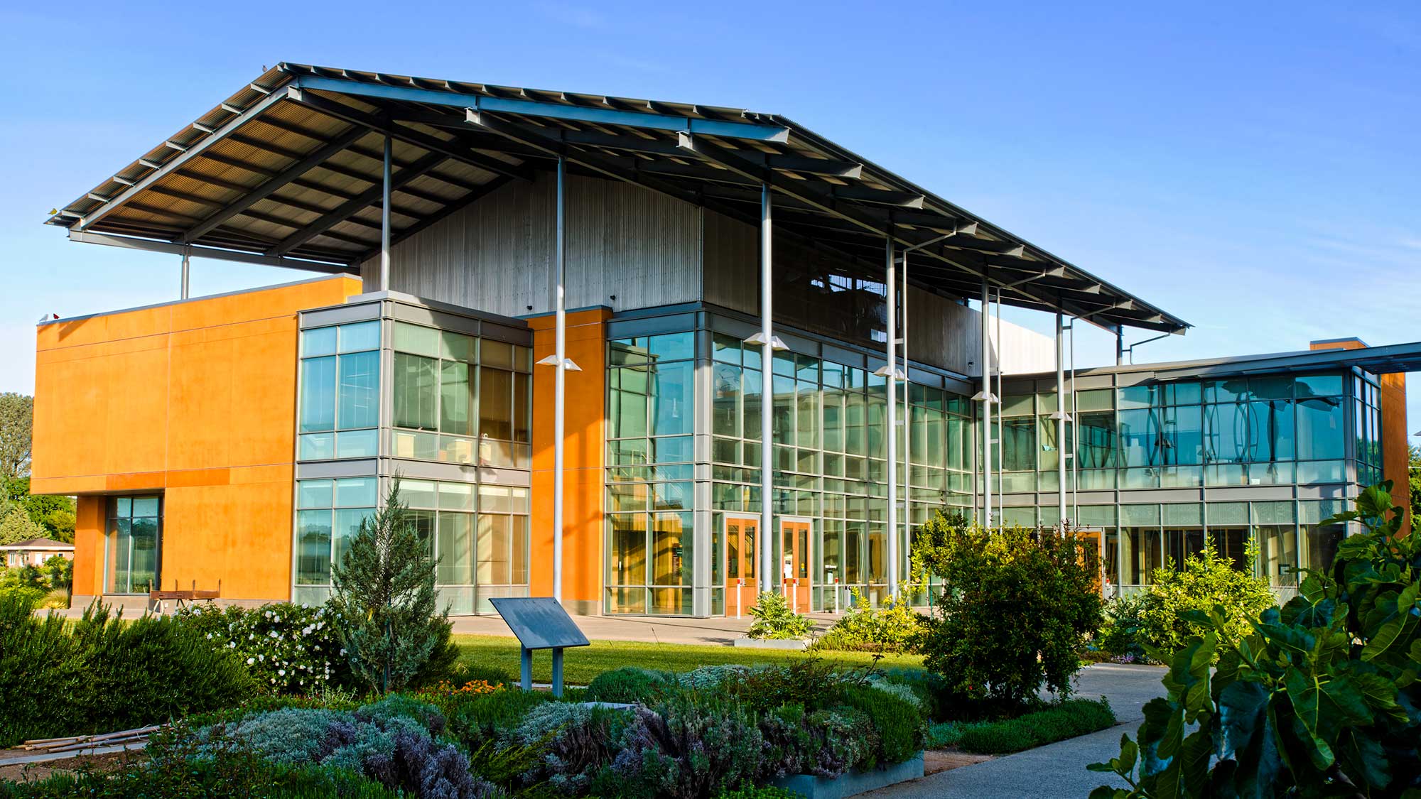 Contemporary glass-and-wood building with large overhang and landscaped foreground, blue sky