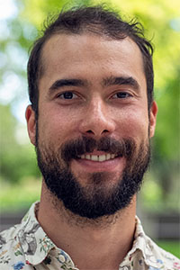 Smiling bearded man wearing a floral shirt, outdoor green blurred background
