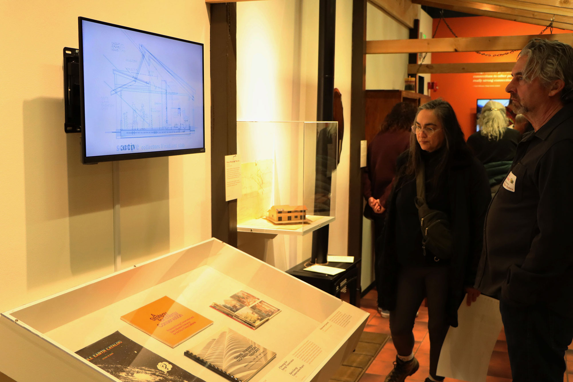 Visitors observing an exhibit with a screen and display case of books.