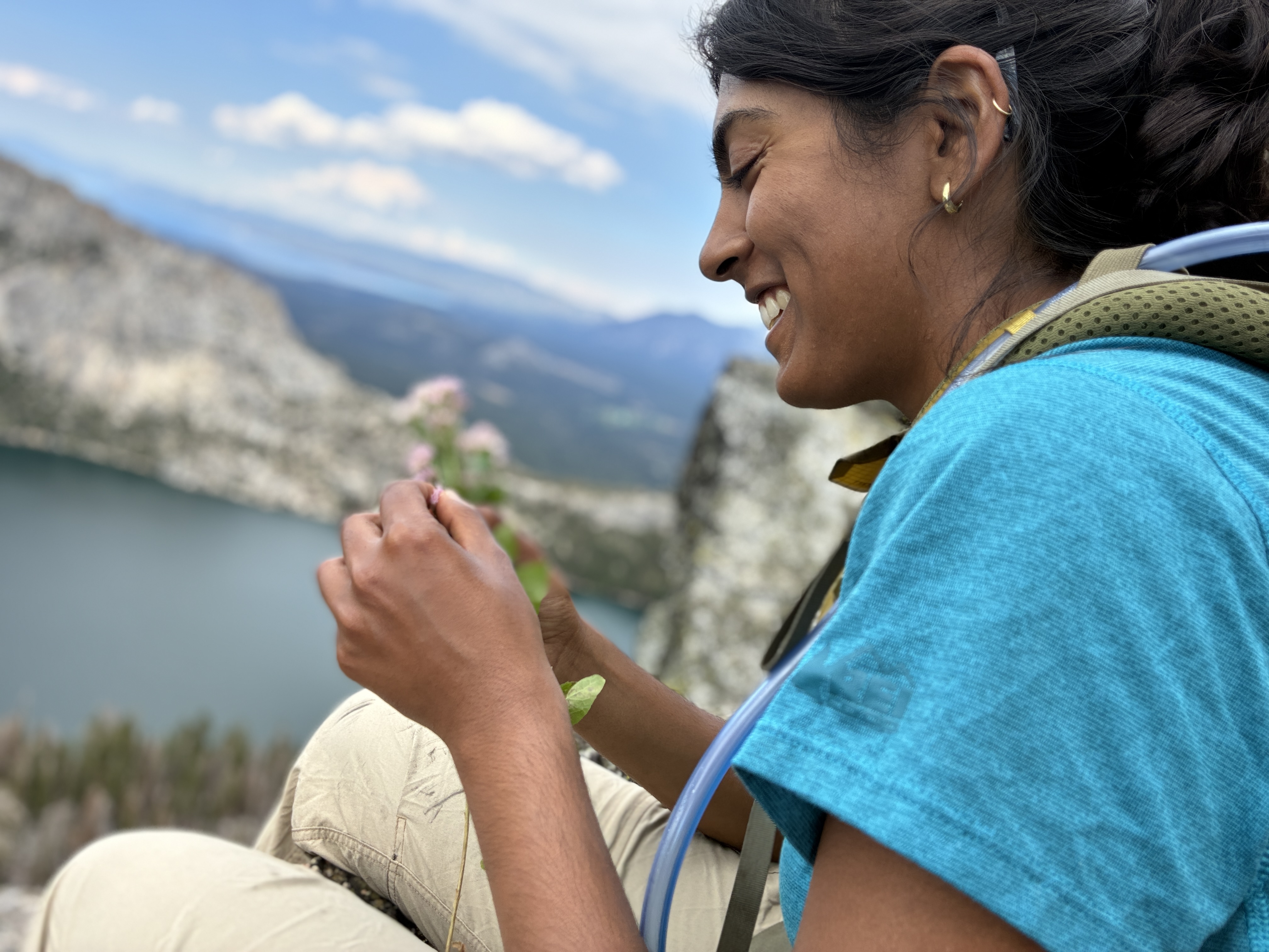 Sachi Srivastava, seen from her profile, smiles in blue tee shirt while overlooking mountains and lake. 